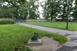 Rzeźba w parku otoczona zielenią i alejką.