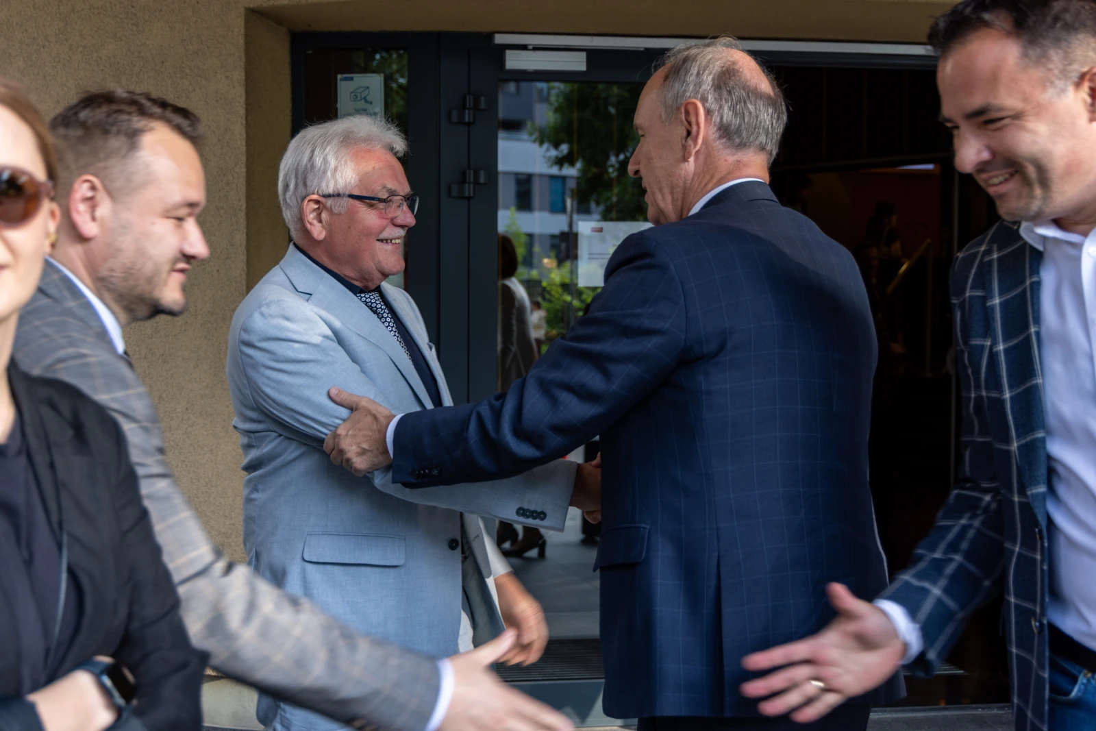 Grupa mężczyzn w garniturach wita się na zewnątrz budynku.  Autor: Bogusław Świerzowski