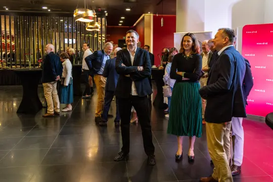 Ludzie w eleganckich strojach rozmawiają w nowoczesnej przestrzeni eventowej.