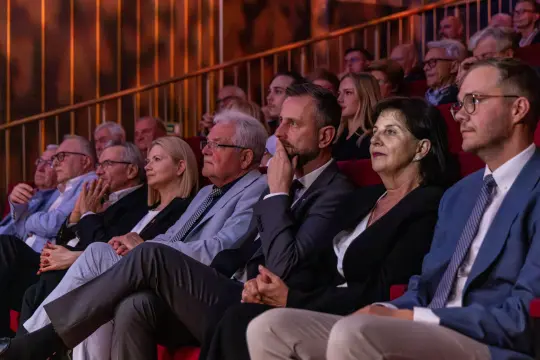 Grupa ludzi siedzących na widowni, skupionych na wydarzeniu kulturalnym.