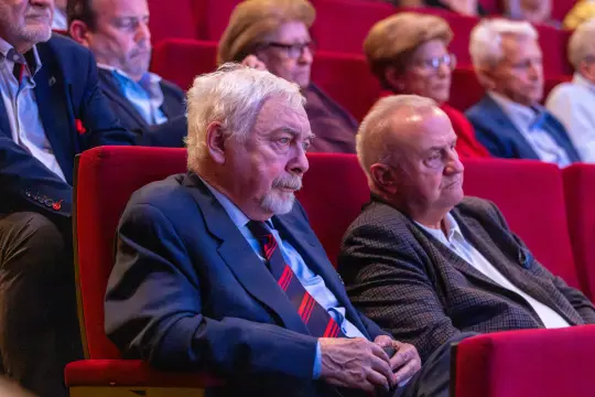 Grupa starszych mężczyzn siedzących na widowni w teatrze.