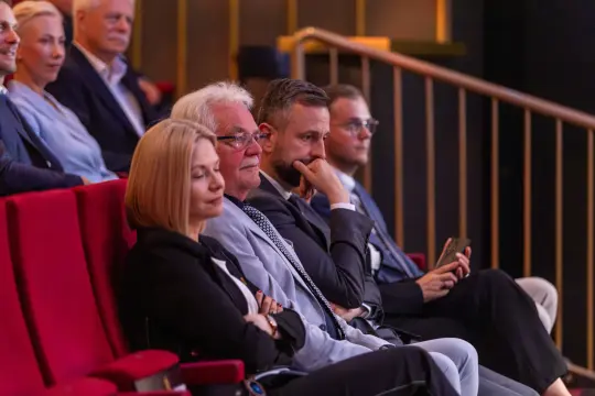 Grupa ludzi siedzących na widowni w teatrze, skupionych na występie.