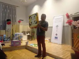 Mężczyzna trzyma planszę edukacyjną podczas prezentacji w sali.
