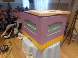 Ul edukacyjny w kolorze różowym i żółtym, otoczony przez grupę osób w tle.