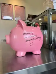 Różowa skarbonka z napisem o zbieraniu funduszy.