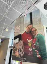 Dwie osoby w swetrach świątecznych pozują obok kolorowych prezentów.