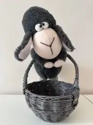Pluszowy owieczka stojąca obok szarego koszyka.