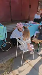 Kobieta rozmawia z dzieckiem siedzącym na krześle przy stoisku z zabawkami.