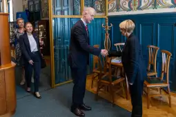 Spotkanie dwóch osób przy uścisku dłoni w eleganckim wnętrzu. W tle inne osoby.