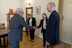 Spotkanie dwóch osób przy uścisku dłoni, w tle kobieta i mężczyzna w formalnych strojach.