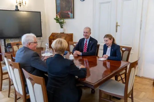 Spotkanie czterech osób przy stole w eleganckim wnętrzu.