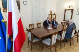 Spotkanie w sali konferencyjnej z flagami Polski i UE w tle.