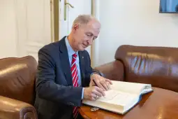 Mężczyzna w garniturze podpisuje dokumenty przy stole.