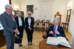 Spotkanie czterech osób w biurze, jedna z nich przy biurku z otwartą księgą.