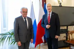 Dwaj mężczyźni stoją obok siebie, za nimi flagi Rosji i Polski.