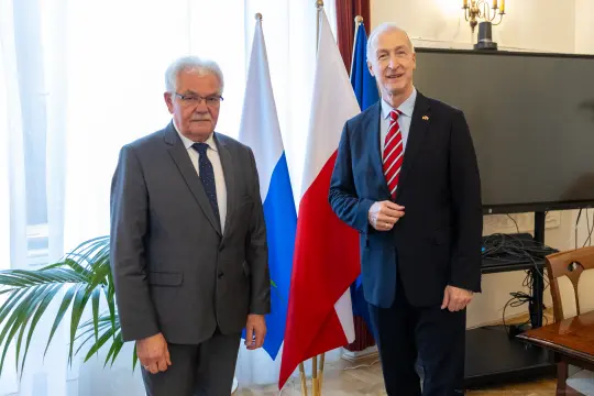 Dwaj mężczyźni stoją obok siebie, za nimi flagi Rosji i Polski.