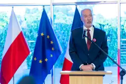 Mężczyzna przemawia przy mównicy, obok flagi Polski, Unii Europejskiej i Francji.