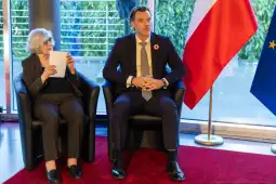 Dwoje ludzi siedzących na kanapie, obok flagi Polski i Unii Europejskiej.