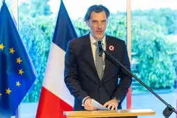 Mężczyzna w garniturze przemawia przy mównicy, obok flagi Francji i Unii Europejskiej.
