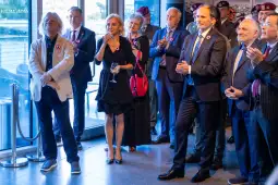 Grupa elegancko ubranych osób na wydarzeniu, niektórzy trzymają kieliszki.