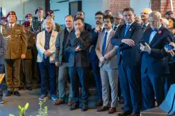 Grupa mężczyzn w garniturach i mundurach, z zainteresowaniem obserwujących wydarzenie.