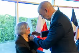 Wręczenie odznaczenia kobiecie przez mężczyznę w eleganckim otoczeniu.