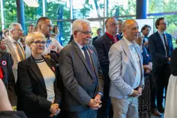 Grupa ludzi w eleganckich strojach, z przypinkami, uczestniczy w wydarzeniu.