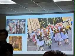 Grupa kobiet w tradycyjnych strojach ludowych niesie kwiaty podczas parady.