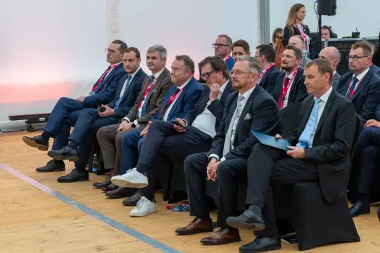 Grupa mężczyzn w garniturach siedzących w rzędzie podczas wydarzenia.
