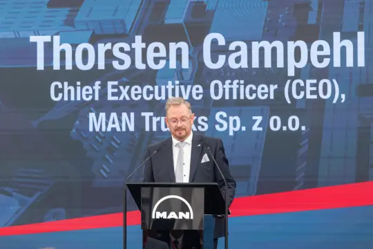 Mężczyzna w garniturze przemawia z podium z logo MAN.