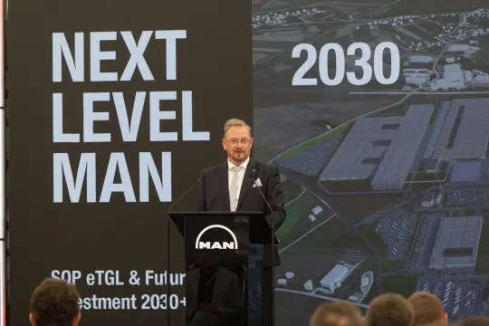 Mężczyzna przemawia na tle prezentacji dotyczącej przyszłości inwestycji MAN do 2030 roku.