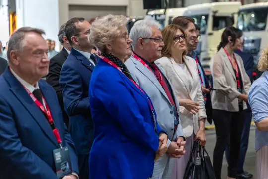 Grupa ludzi w formalnych strojach, uczestniczących w wydarzeniu branżowym.