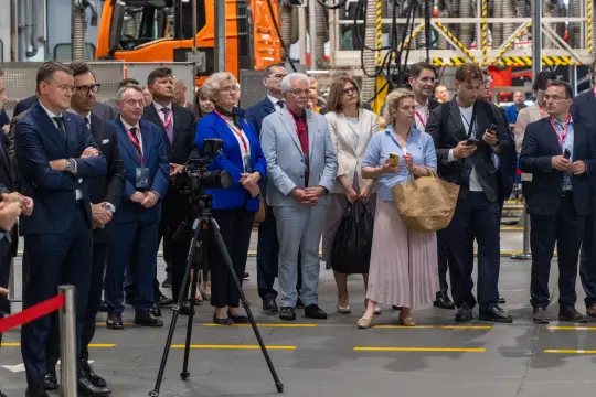 Grupa ludzi w formalnych strojach podczas wydarzenia przemysłowego.