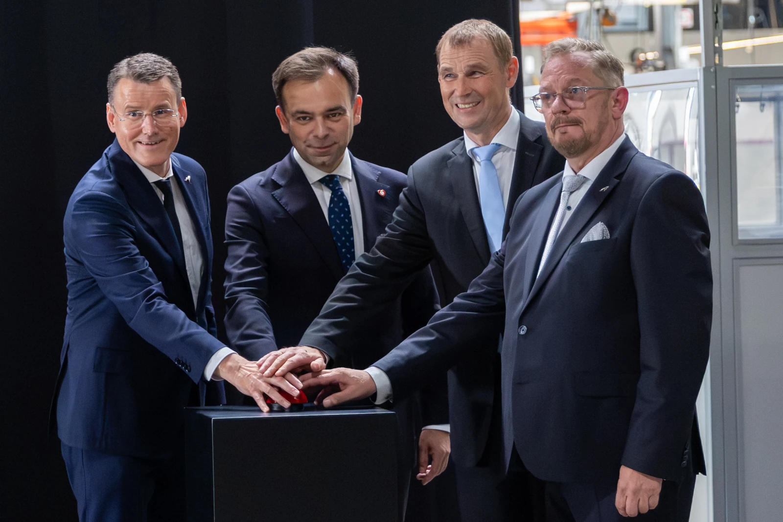 Czterech mężczyzn w garniturach, wspólnie naciskających przycisk na podium.  Autor: Bogusław Świerzowski