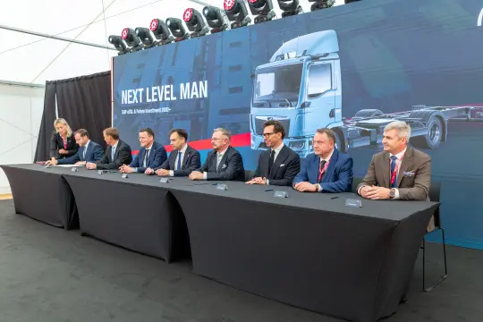Siedmiu mężczyzn w garniturach przy stole konferencyjnym, prezentacja nowego modelu ciężarówki.