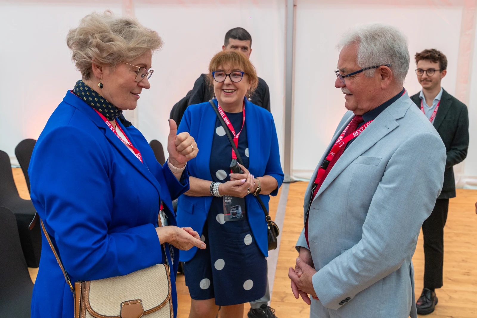 Trzy osoby w rozmowie, jedna z nich gestykuluje, wszyscy uśmiechnięci, w eleganckich strojach.  Autor: Bogusław Świerzowski