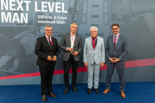 Czterech mężczyzn w garniturach na tle grafiki promującej inwestycje w przyszłość.
