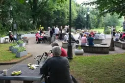 Grupa osób spędza czas w parku, rozmawiając i relaksując się w otoczeniu zieleni.