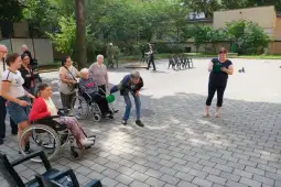 Grupa osób w różnym wieku bawi się na świeżym powietrzu, niektórzy w wózkach inwalidzkich.