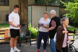 Młody mężczyzna rozmawia z dwiema starszymi kobietami w parku.