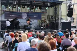 Koncert na świeżym powietrzu z muzykami grającymi na scenie przed publicznością.