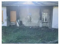 Zniszczona elewacja budynku z zasłoniętymi oknami i porośniętym trawnikiem.