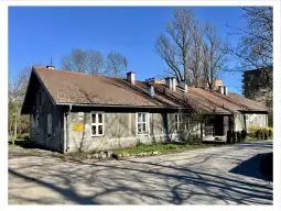 Budynek mieszkalny z jasnymi ścianami i czerwonym dachem, otoczony drzewami i zielenią.