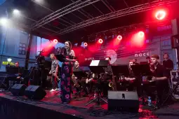 Koncert na scenie z muzykami i wokalistką w kolorowych światłach.