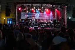 Koncert na scenie z zespołem i publicznością, oświetlenie w kolorach czerwonym i niebieskim.
