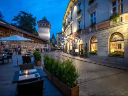 Urokliwa uliczka z oświetlonymi budynkami i wieżą w tle.