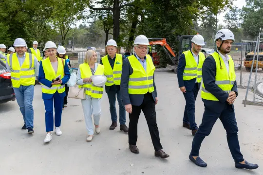 Grupa osób w kamizelkach odblaskowych i kaskach na placu budowy.
