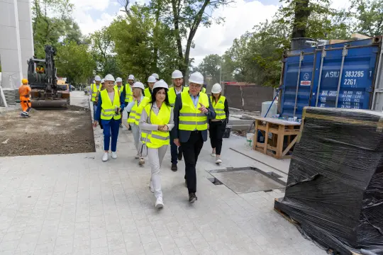 Grupa osób w kaskach i kamizelkach odblaskowych na placu budowy.