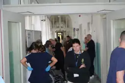 Grupa ludzi w szpitalnym korytarzu, personel medyczny i pacjenci.