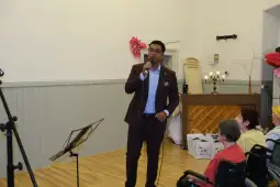 Mężczyzna śpiewa na scenie, w tle publiczność i instrumenty muzyczne.